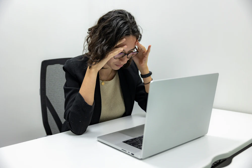 A woman at her laptop holding her head, struggling to focus
